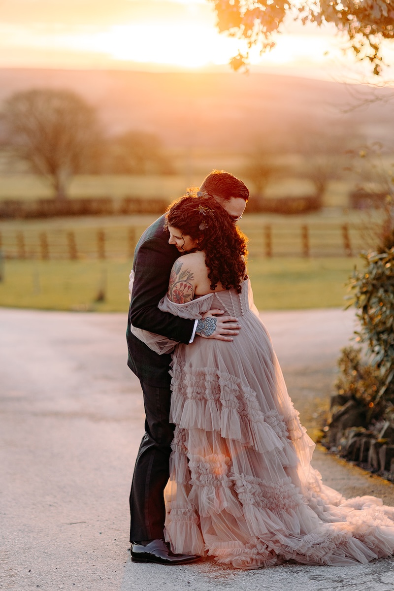 Couple hugging beneath the golden sunset sky at The Wellbeing Farm, photographed by their wedding photographer.