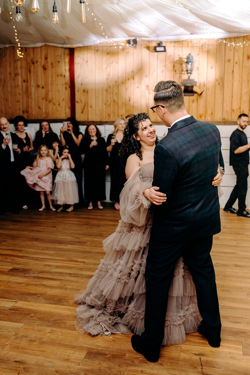 Couple dancing closely together during their first dance surrounded by guests at The Wellbeing Farm.
