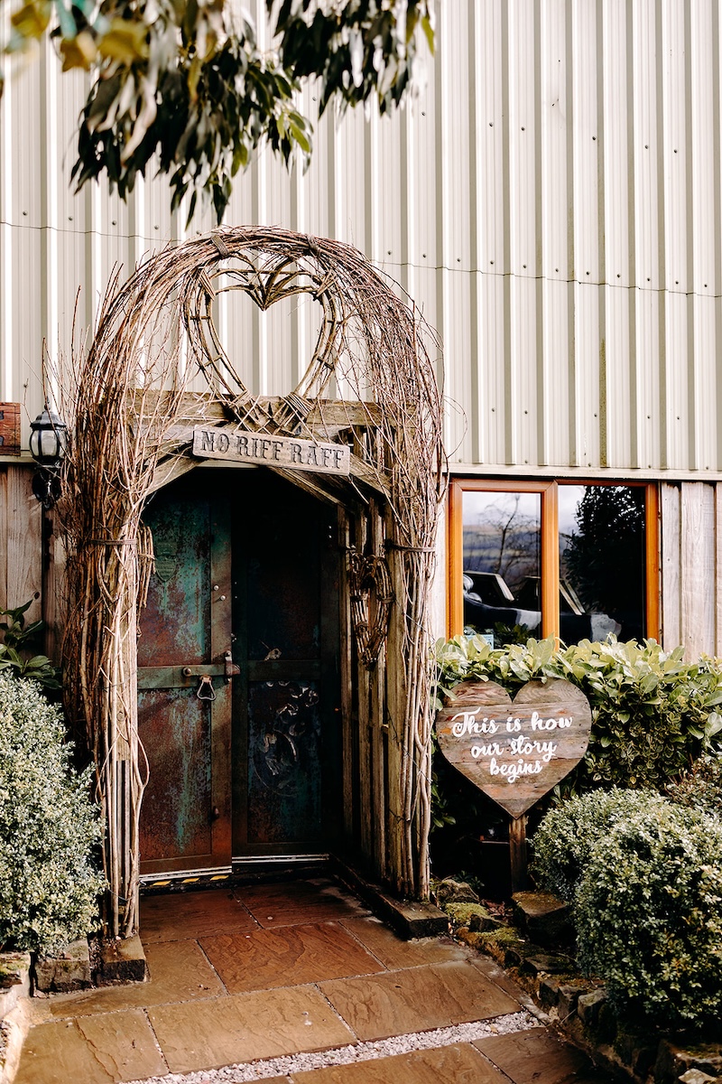 Rustic barn entrance decorated with greenery at The Wellbeing Farm sustainable wedding venue, photographed as part of relaxed Wellbeing Farm wedding photography.
