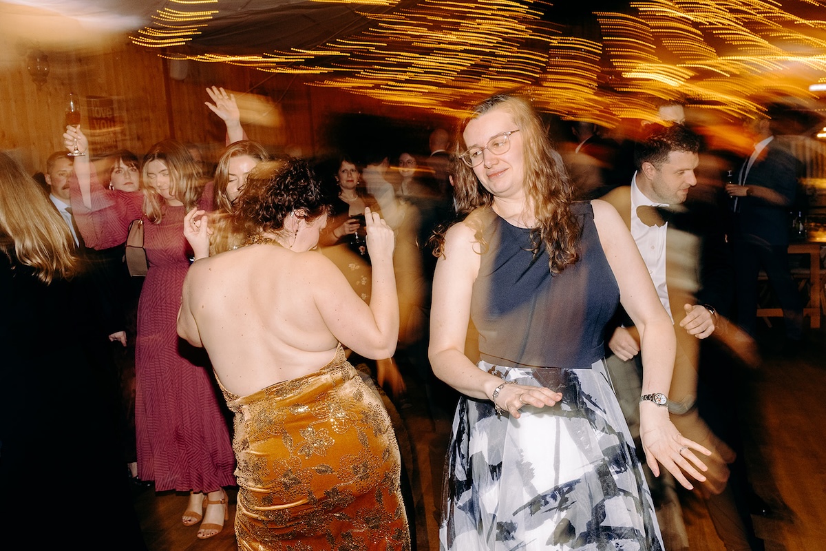 Guests dancing enthusiastically beneath the fairy lights during the evening wedding celebration.
