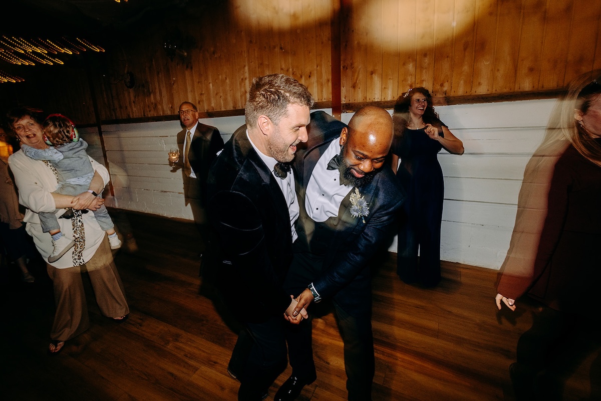 Wedding guests dancing together under the warm fairy lights inside the barn reception space.