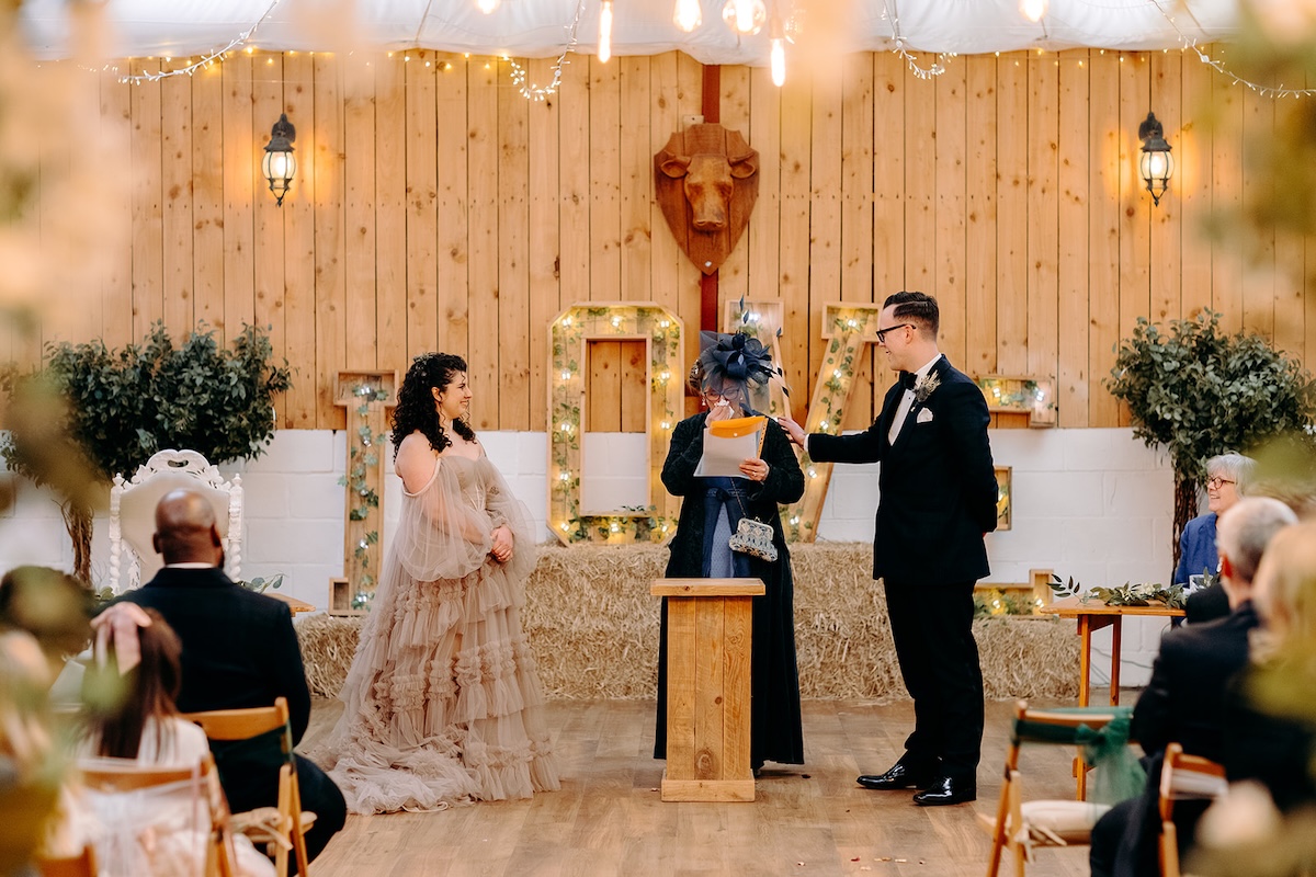 Bride and groom standing together beneath the greenery ceremony arch at The Wellbeing Farm during their February wedding, captured with documentary wedding photography.