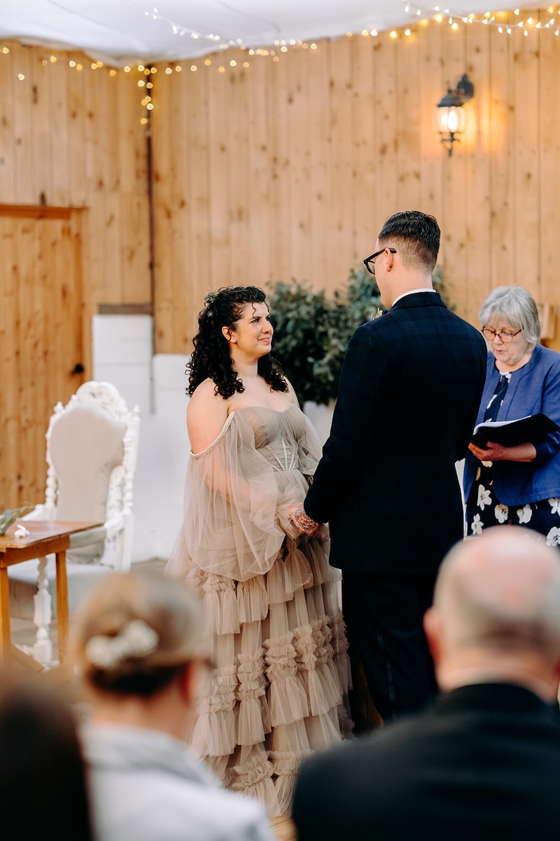 Bride and groom standing together at the altar inside the decorated barn venue at The Wellbeing Farm, captured with relaxed wedding photography.