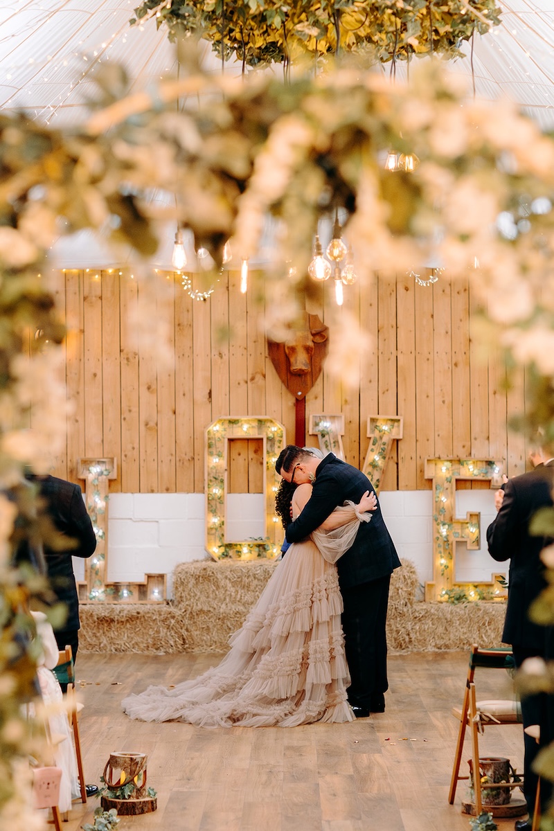 Bride and groom sharing their first kiss beneath the floral ceremony arch at their February wedding.