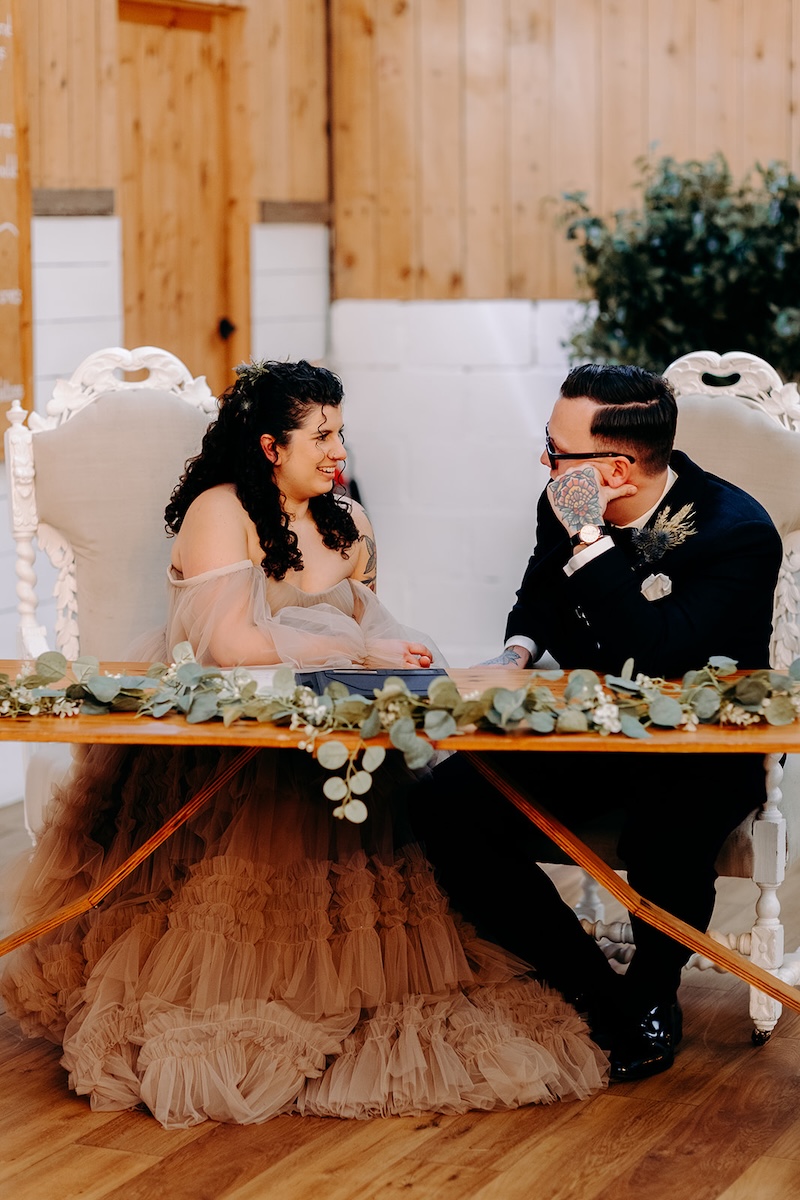 Bride and groom seated at the signing table during their ceremony at The Wellbeing Farm.