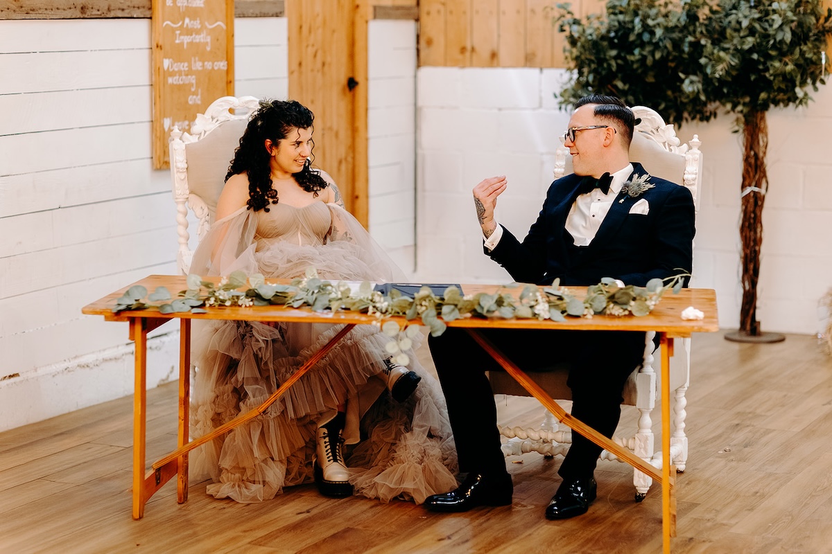 Bride and groom laughing together while signing their marriage register.