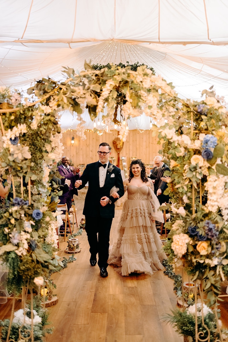 Bride and groom walking back down the aisle beneath the floral arch after their ceremony at The Wellbeing Farm.