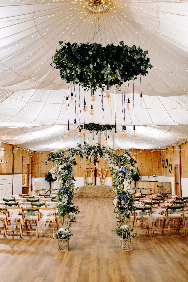 Ceremony space inside The Wellbeing Farm barn with floral arch and guest seating ready for a February winter wedding, photographed with documentary wedding photography.