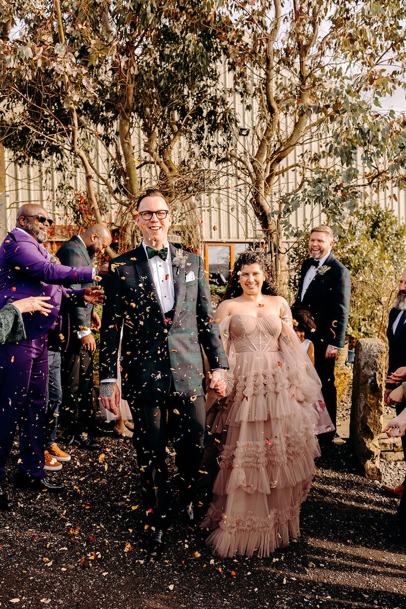 Bride and groom smiling while confetti falls around them after their February wedding ceremony.