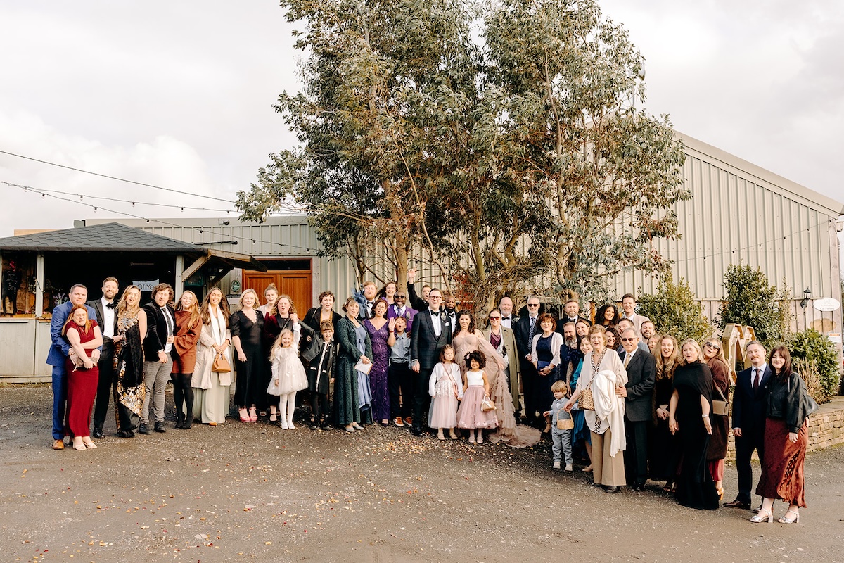 Large group of wedding guests gathered outside the barn for a group photo at The Wellbeing Farm.