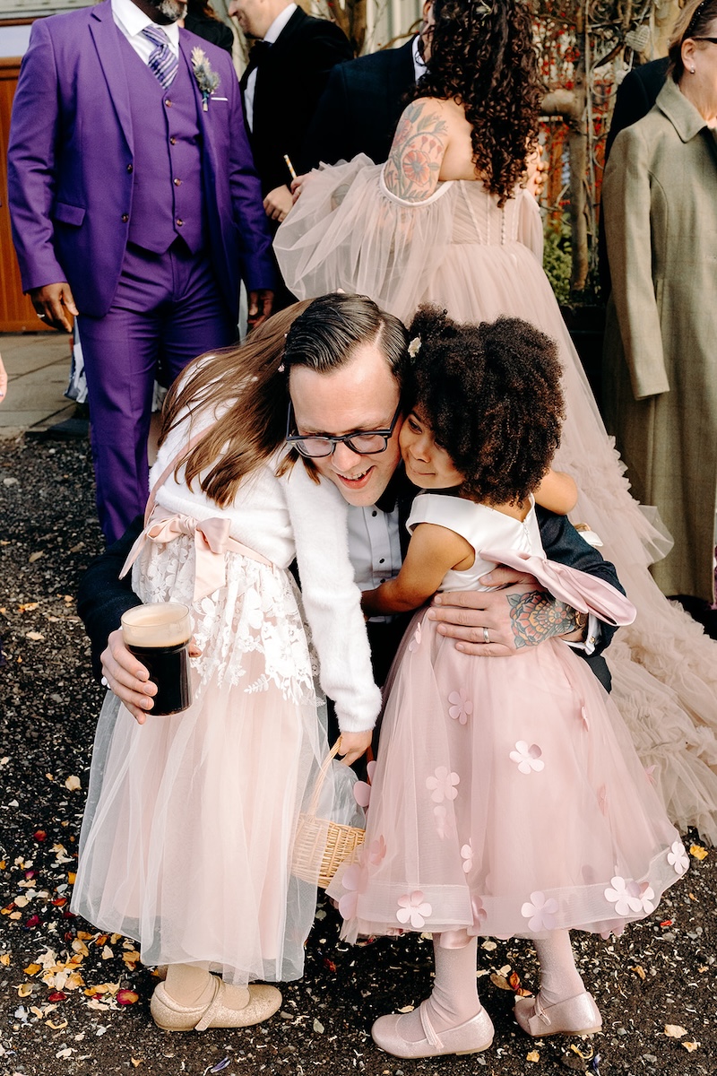 Young flower girl hugging the groom during the confetti celebration.