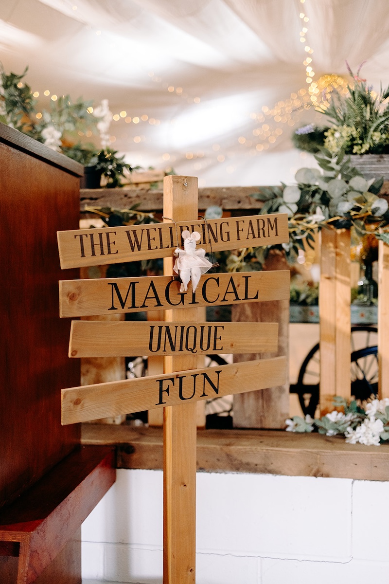 Wooden welcome sign reading “The Wellbeing Farm Magical Unique Fun” inside the barn venue, captured as part of relaxed Wellbeing Farm wedding photography.