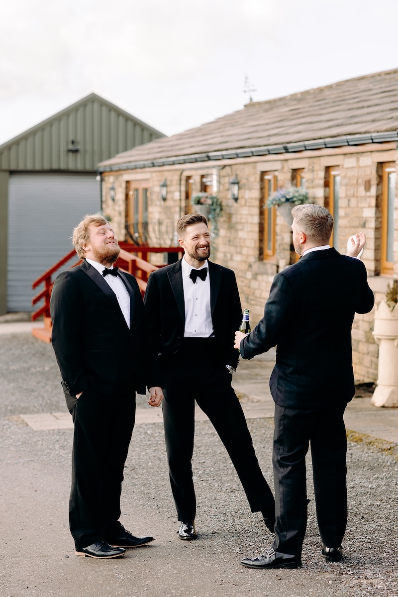Groom and groomsmen chatting outside the barn courtyard during the winter wedding reception.