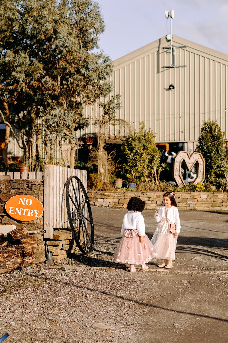 Flower girls walking across the courtyard outside the barn after the ceremony.