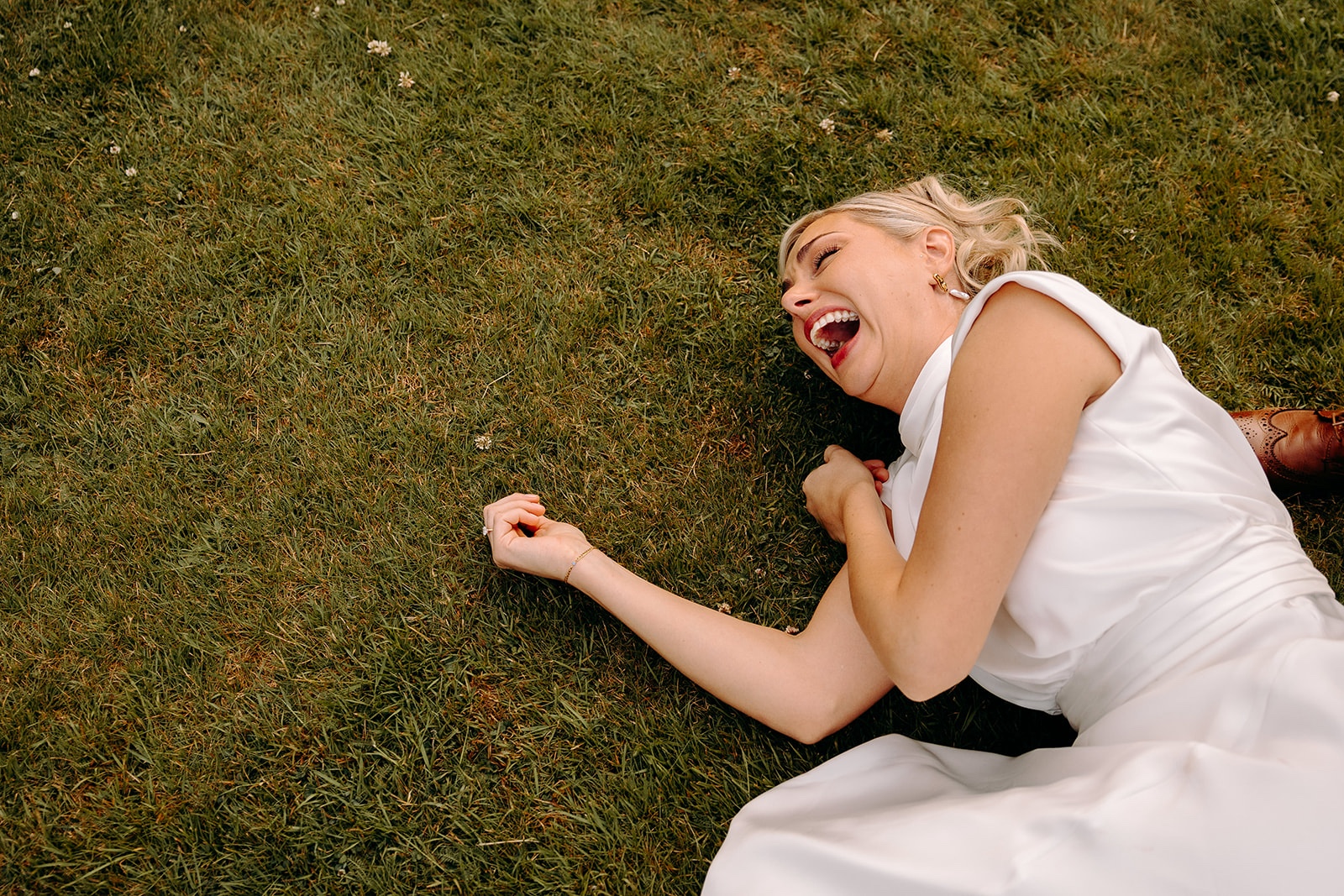 Bride lying on the grass laughing during relaxed couple portraits in the evening sunshine.