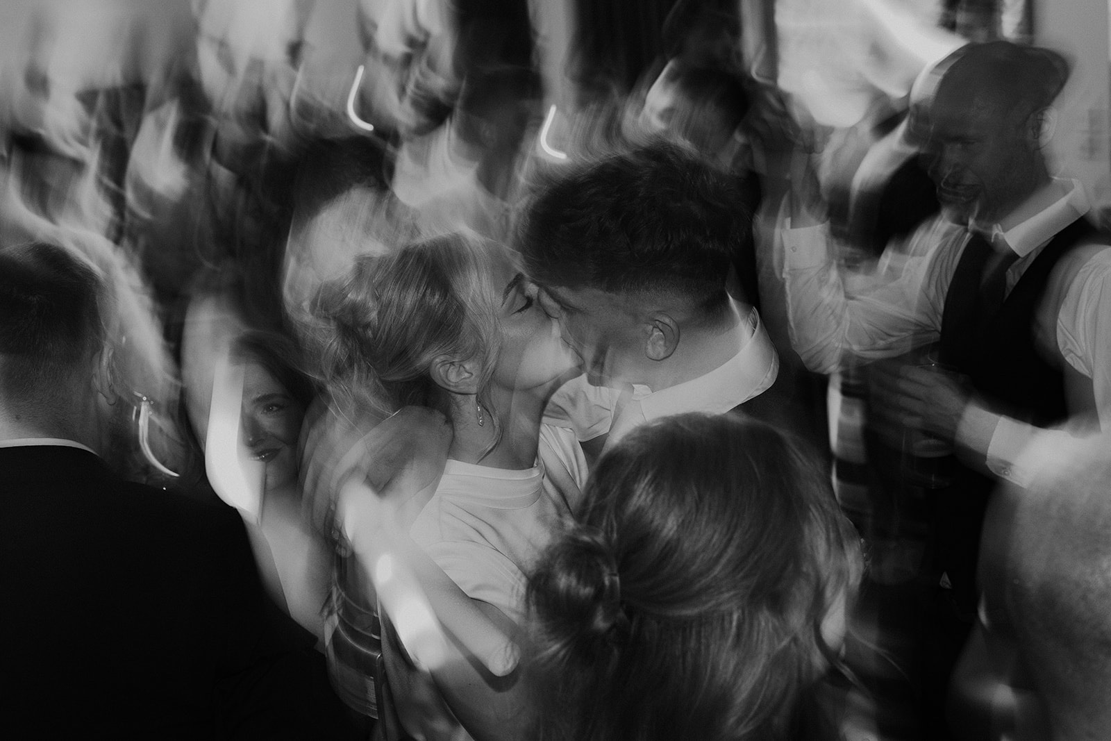 Black and white photograph capturing the chaos of a packed wedding dance floor.