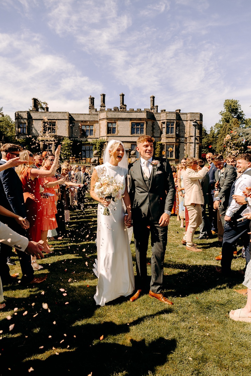 Just-married couple surrounded by guests in the gardens of Thornbridge Hall.