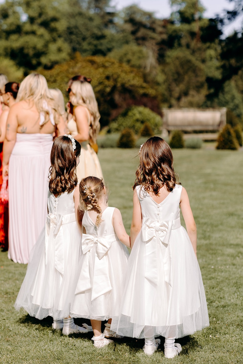 Flower girls walking across the lawn during a summer wedding at Thornbridge Hall.